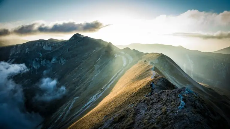 A breathtaking view of the Sibillini Mountains at sunrise with golden sunlight casting over the peaks.